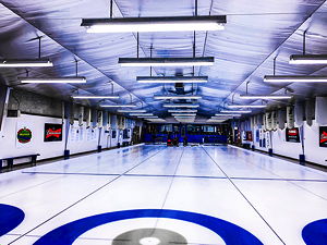 A curling hall with three lanes, people standing at the start preparing 